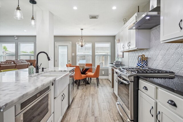 kitchen featuring wall chimney range hood, a sink, light wood finished floors, stainless steel appliances, and visible vents
