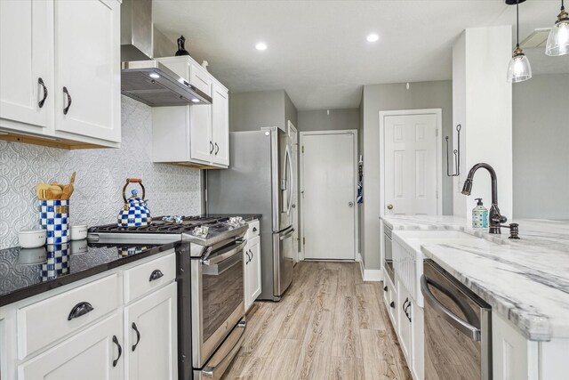 kitchen with appliances with stainless steel finishes, light wood-type flooring, light stone counters, white cabinets, and wall chimney exhaust hood