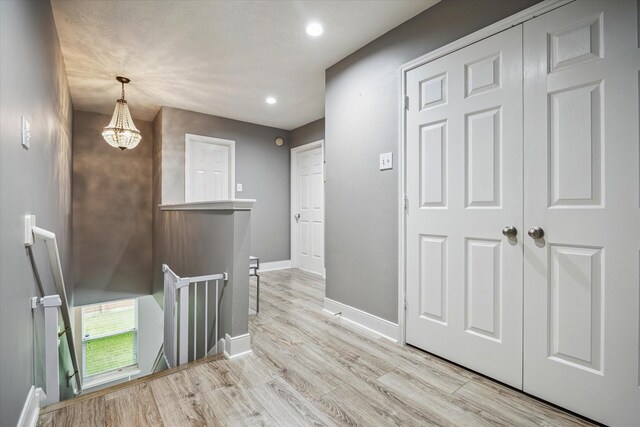 hall with an inviting chandelier, light wood-style floors, recessed lighting, baseboards, and an upstairs landing