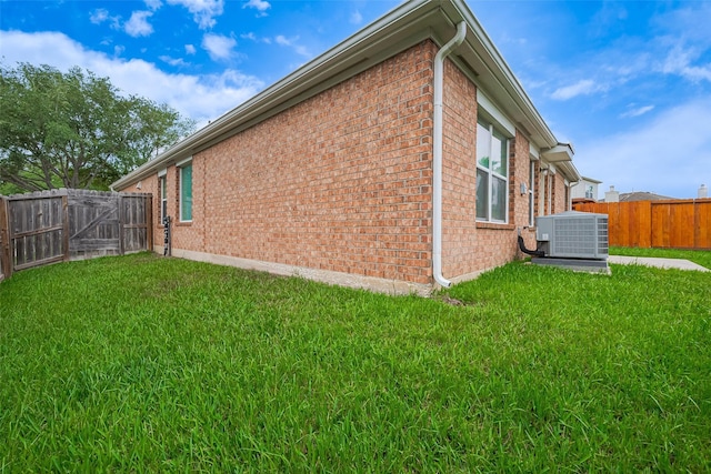 view of side of property featuring brick siding, central AC unit, a gate, and a fenced backyard