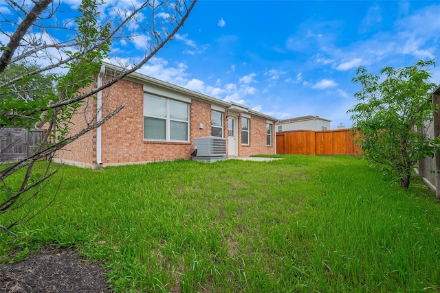 rear view of house with a yard, brick siding, a fenced backyard, and central air condition unit