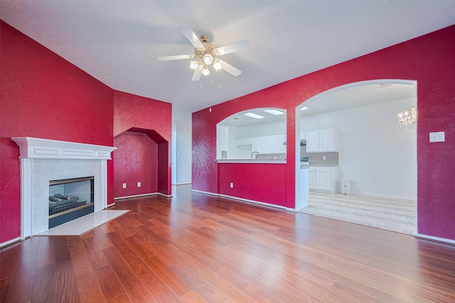 526 Majestic Ridge Dr, Houston, TX 77049 - unfurnished living room featuring ceiling fan, a fireplace with flush hearth, arched walkways, wood finished floors, and a sink