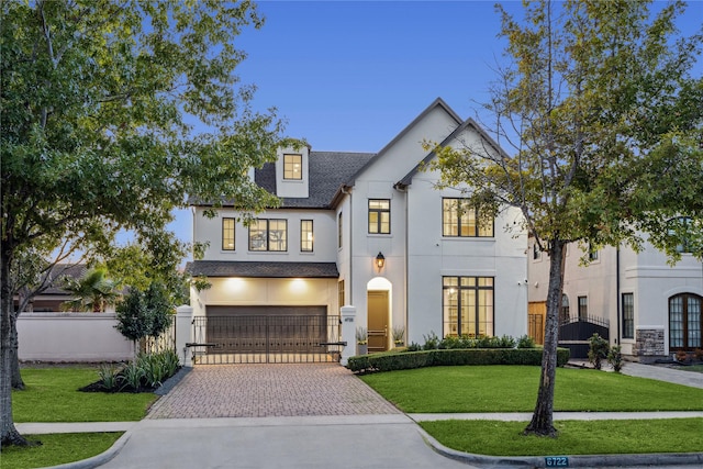 french country inspired facade featuring a garage, a front lawn, fence, decorative driveway, and stucco siding