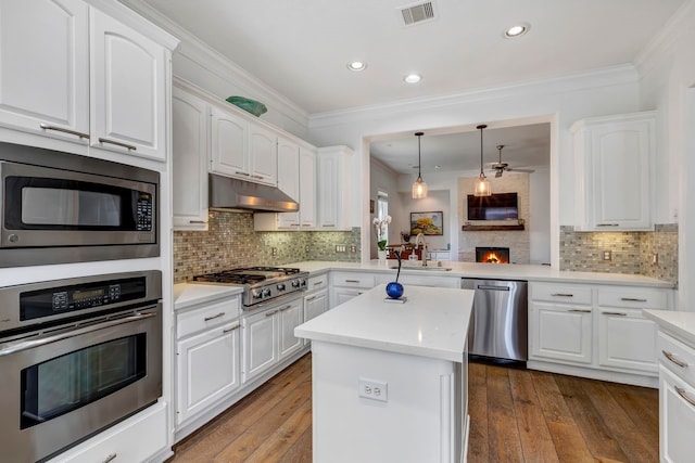 1267 Sopris Dr, Houston, TX 77077 - kitchen with appliances with stainless steel finishes, a sink, under cabinet range hood, a warm lit fireplace, and white cabinets