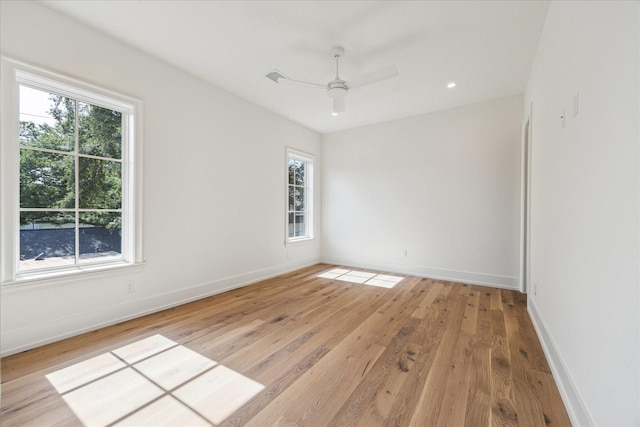 spare room featuring plenty of natural light, light wood finished floors, ceiling fan, and baseboards