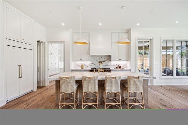 4230 Whitman St, Houston, TX 77027 - kitchen with decorative backsplash, light wood-style floors, white cabinetry, pendant lighting, and an island with sink