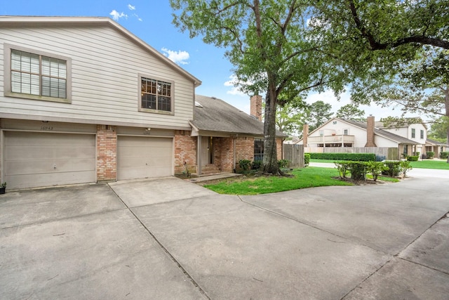 view of front of house featuring a garage, fence, a chimney, brick siding, and driveway