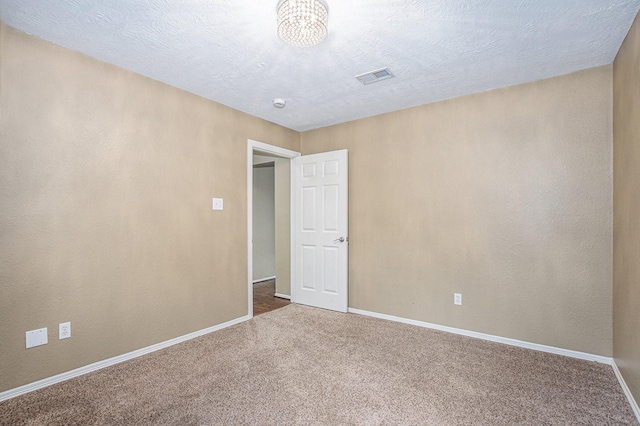 carpeted spare room featuring visible vents, a textured ceiling, and baseboards