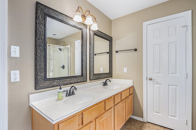 full bathroom featuring double vanity, a textured wall, a shower stall, and a sink