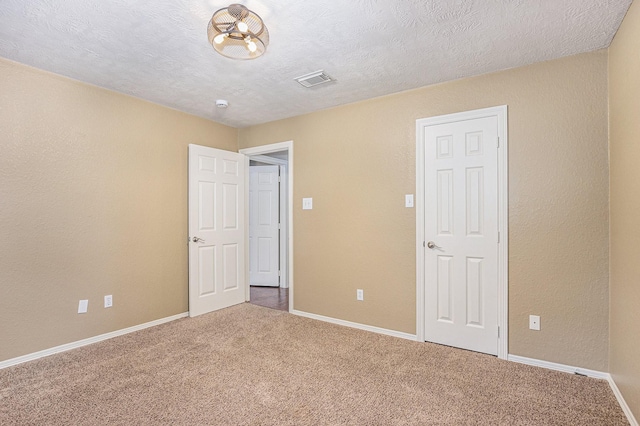 unfurnished bedroom featuring carpet floors, a textured ceiling, baseboards, and visible vents