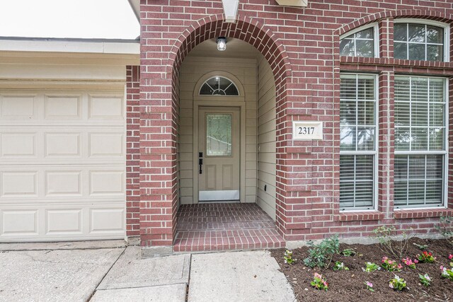 view of exterior entry with a garage and brick siding