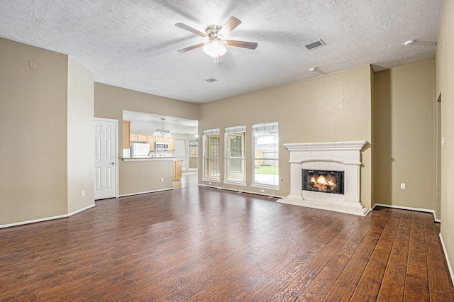 unfurnished living room featuring ceiling fan, a textured ceiling, visible vents, a warm lit fireplace, and dark wood-style floors