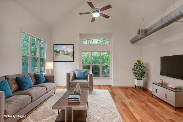 living room featuring baseboards, light wood finished floors, ceiling fan, and high vaulted ceiling