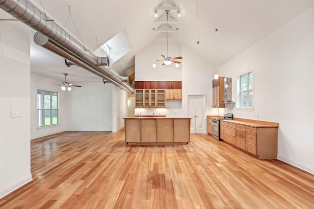 kitchen with high vaulted ceiling, stainless steel gas range, a ceiling fan, and wall chimney exhaust hood