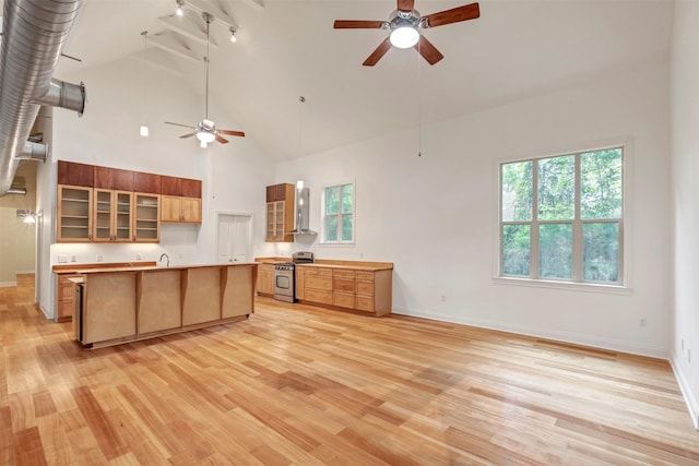 11958 White Oak Path, Conroe, TX 77385 - kitchen with stainless steel range with gas cooktop, a ceiling fan, wall chimney range hood, light wood-type flooring, and high vaulted ceiling