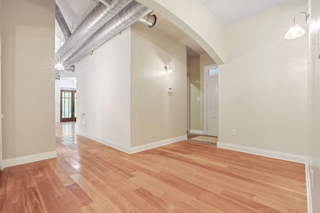 spare room featuring light wood-type flooring, arched walkways, and baseboards
