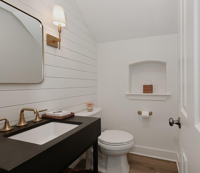 bathroom with vaulted ceiling, wood finished floors, vanity, baseboards, and toilet