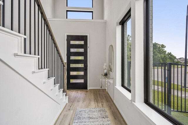 foyer featuring a high ceiling, a healthy amount of sunlight, stairway, and wood finished floors