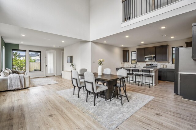 dining space featuring recessed lighting, light wood-type flooring, and a towering ceiling