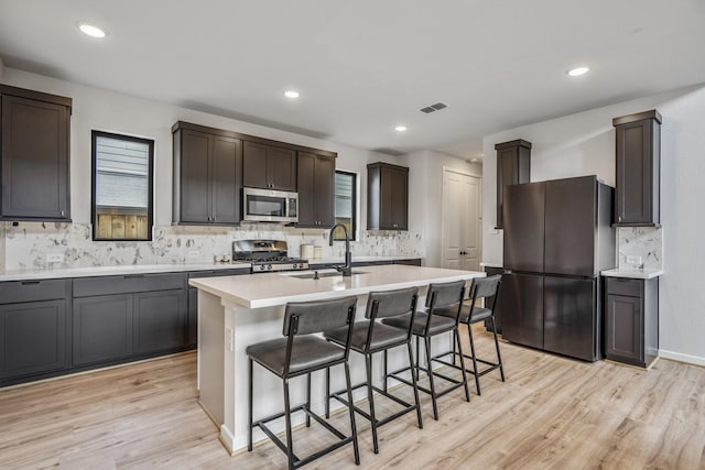 kitchen featuring visible vents, decorative backsplash, a breakfast bar, a sink, and appliances with stainless steel finishes