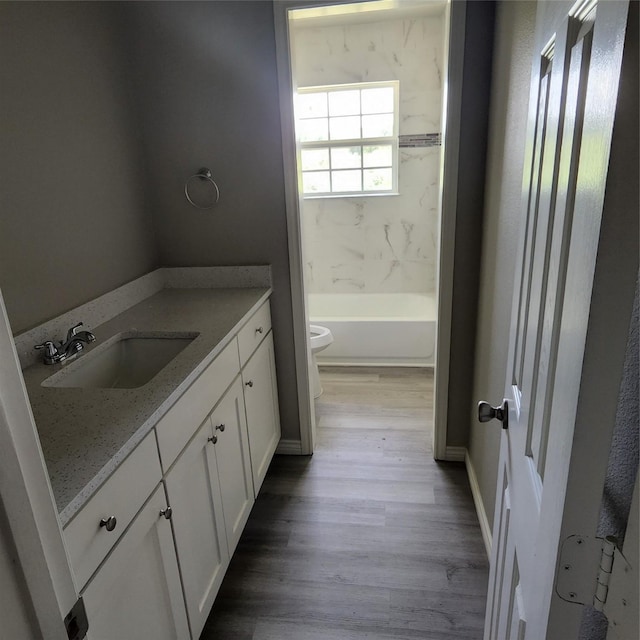 bathroom featuring wood finished floors, vanity, baseboards, toilet, and bathing tub / shower combination