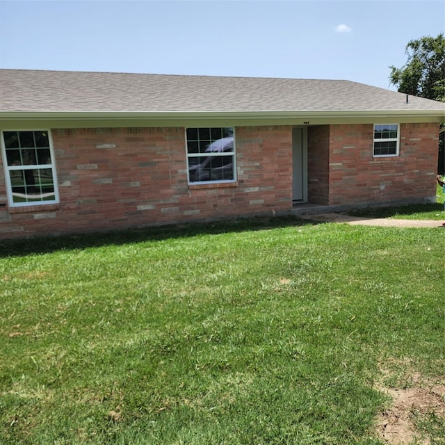 view of front of property featuring roof with shingles, a front lawn, and brick siding