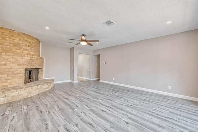 unfurnished living room featuring visible vents, wood finished floors, a fireplace, baseboards, and a ceiling fan