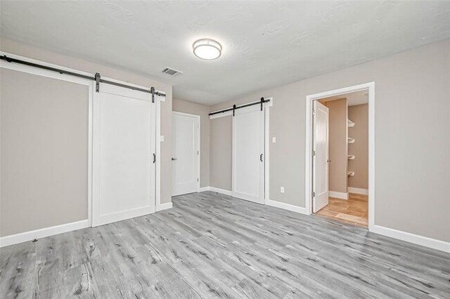 unfurnished bedroom featuring a barn door, light wood-style flooring, baseboards, ensuite bathroom, and visible vents