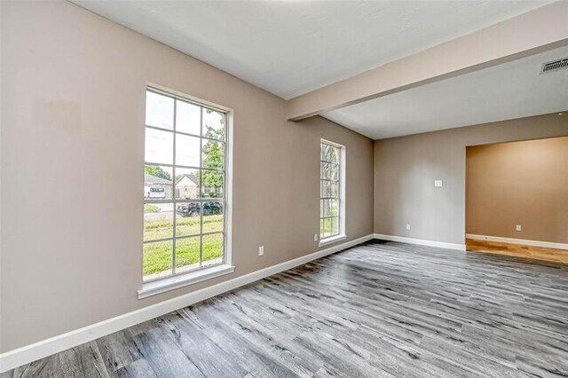empty room featuring baseboards, beam ceiling, wood finished floors, and visible vents