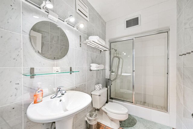 bathroom with visible vents, an enclosed shower, tile walls, a sink, and toilet