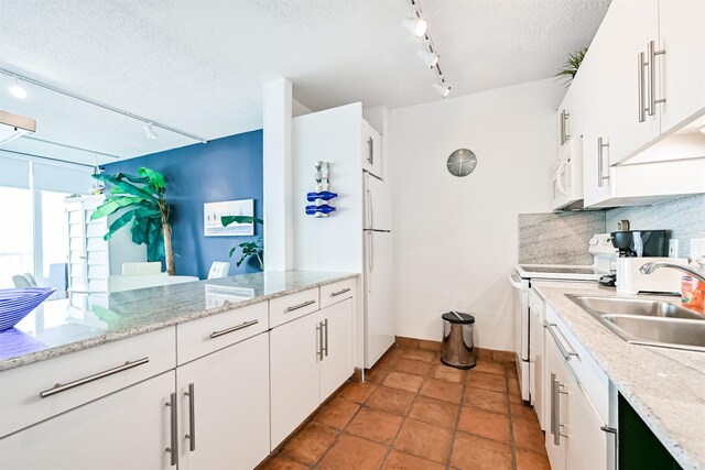 kitchen featuring track lighting, a sink, white appliances, a textured ceiling, and baseboards