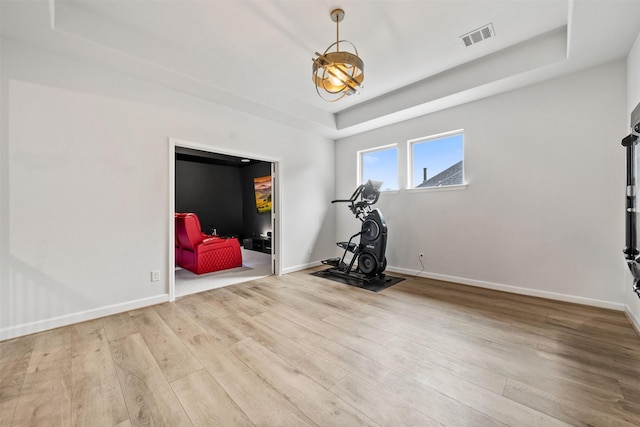 exercise area featuring baseboards, a tray ceiling, wood finished floors, and visible vents