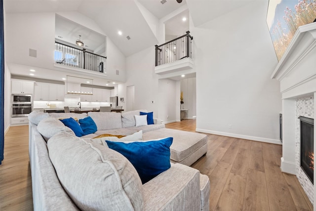 living area with light wood finished floors, high vaulted ceiling, a glass covered fireplace, a ceiling fan, and baseboards