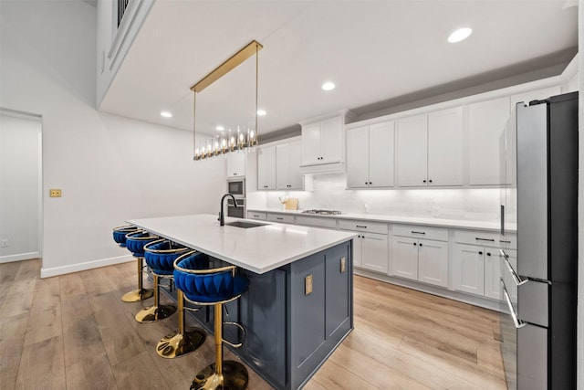 kitchen featuring a kitchen island with sink, a sink, light wood finished floors, stainless steel appliances, and white cabinetry