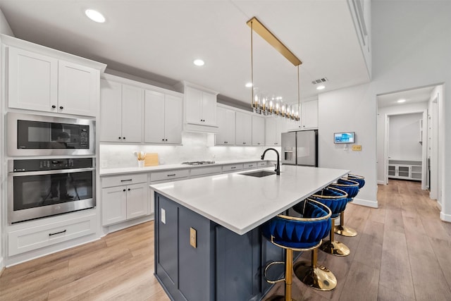 kitchen with a sink, light wood-style floors, stainless steel appliances, and white cabinetry