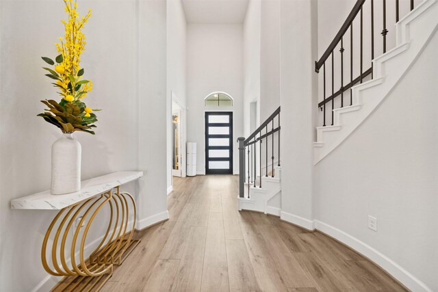 entryway featuring stairs, baseboards, wood finished floors, and a towering ceiling