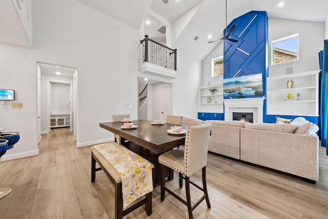dining area featuring a glass covered fireplace, baseboards, high vaulted ceiling, stairway, and light wood finished floors