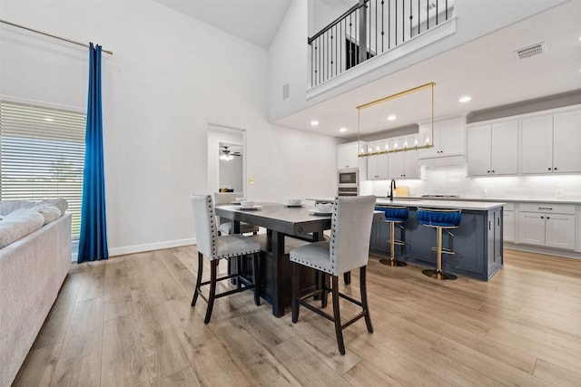 dining room with light wood-style floors, baseboards, a towering ceiling, and visible vents