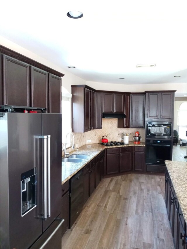 kitchen featuring dark brown cabinets, light stone countertops, light wood-style floors, a sink, and black appliances