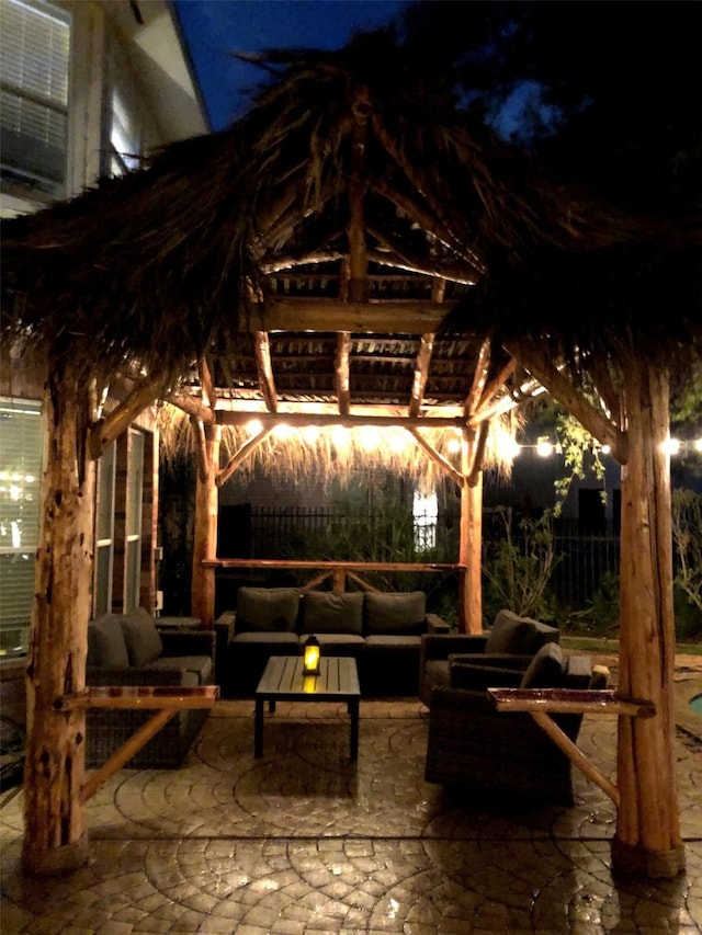 patio at night featuring a gazebo, outdoor lounge area, and fence