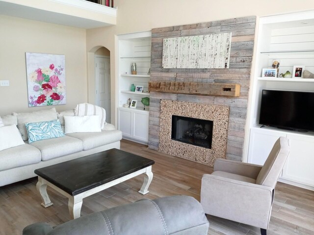 living area with arched walkways, wood finished floors, and a tile fireplace