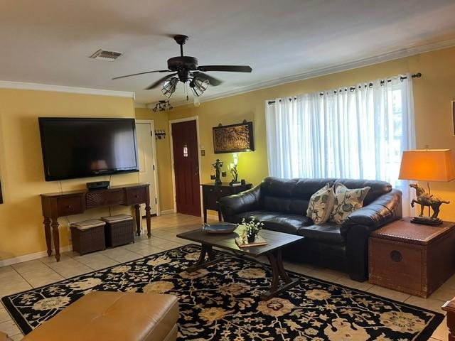 living room with light tile patterned flooring, ceiling fan, baseboards, visible vents, and ornamental molding