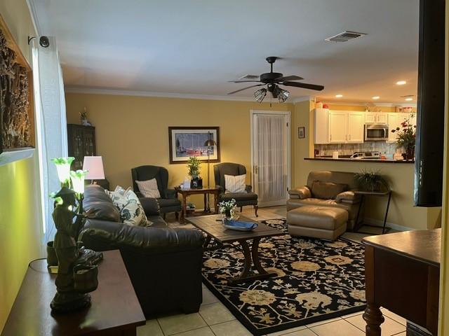 living area with light tile patterned floors, crown molding, a ceiling fan, and visible vents