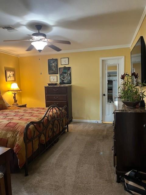 carpeted bedroom with visible vents, ornamental molding, baseboards, and ceiling fan