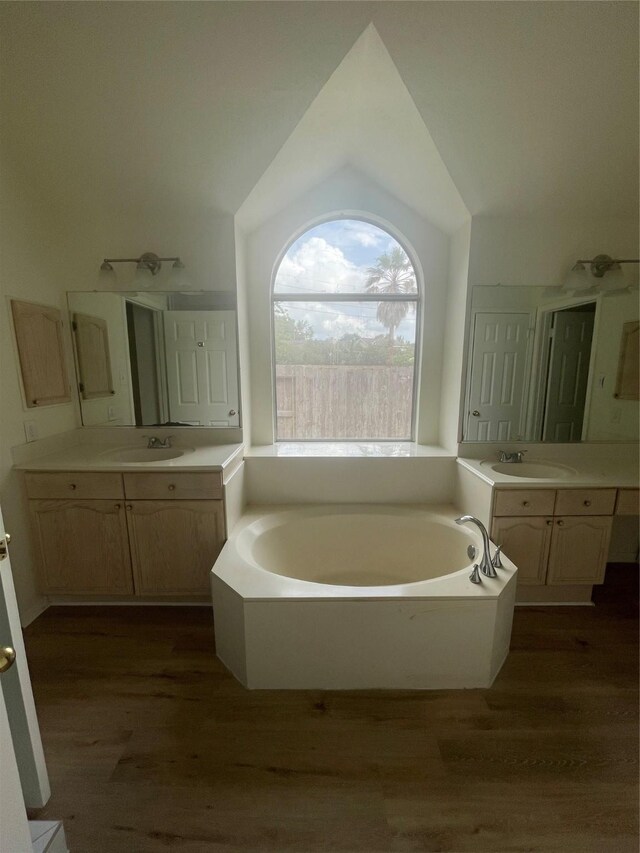 bathroom featuring vaulted ceiling, a sink, a bath, and wood finished floors