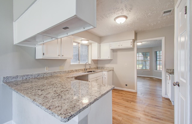 kitchen with a peninsula, light stone countertops, white cabinetry, a sink, and light wood finished floors
