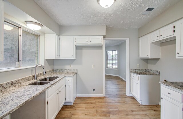 kitchen featuring visible vents, a sink, light stone counters, white cabinets, and baseboards