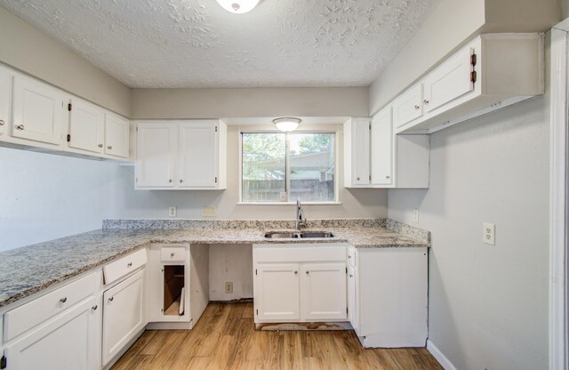 kitchen with a sink, light stone counters, white cabinets, and light wood finished floors
