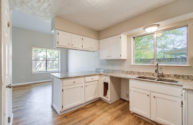 kitchen with a sink, white cabinetry, a peninsula, and light wood finished floors