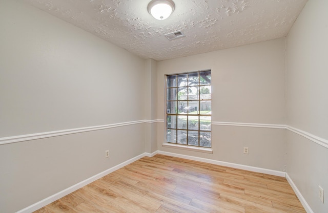 unfurnished room featuring baseboards, a textured ceiling, visible vents, and wood finished floors